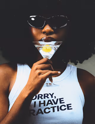 Woman with sunglasses drinking a martini with a branded tank top that says : sorry, I have practice