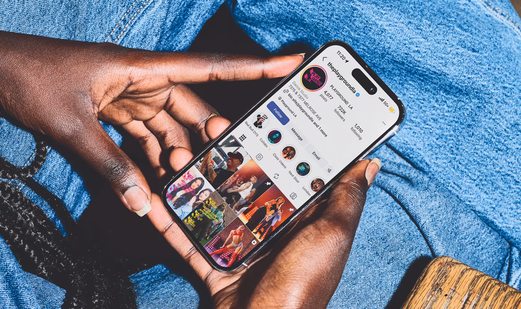 Close up of person holding phone with legs crossed. Mockup of the Playground L.A.'s instagram Page