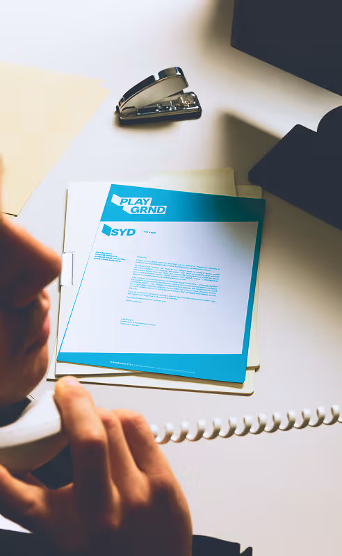 Employee responding to the phone (cable as well) with blue and white sydney (SYD) stationnery letter design on the desk. Mockup source : Bendito Mockups