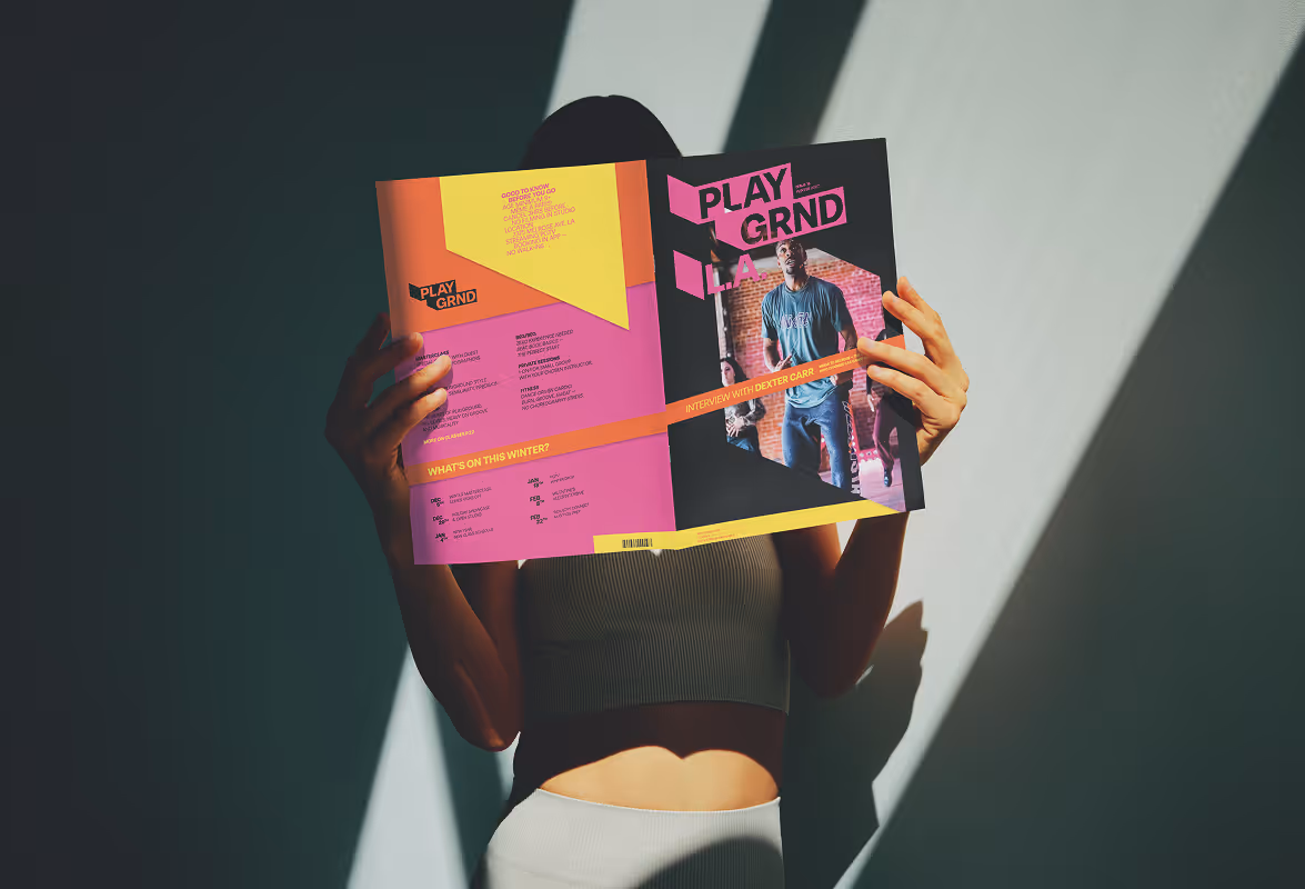 Woman holding a Playground L.A. magazine which hides her face. Shadows highlight the publication. Source : Mockup Maison