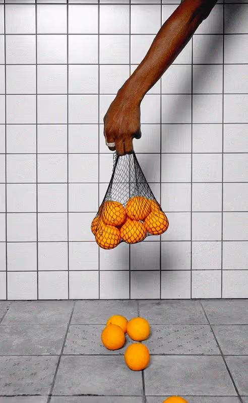 Hand holding a bag of oranges spilling on the floor in front of a tiled black and white kitchen wall. Found on Death to Stock: "hang in there" shot by Cecilia DI PAOLO